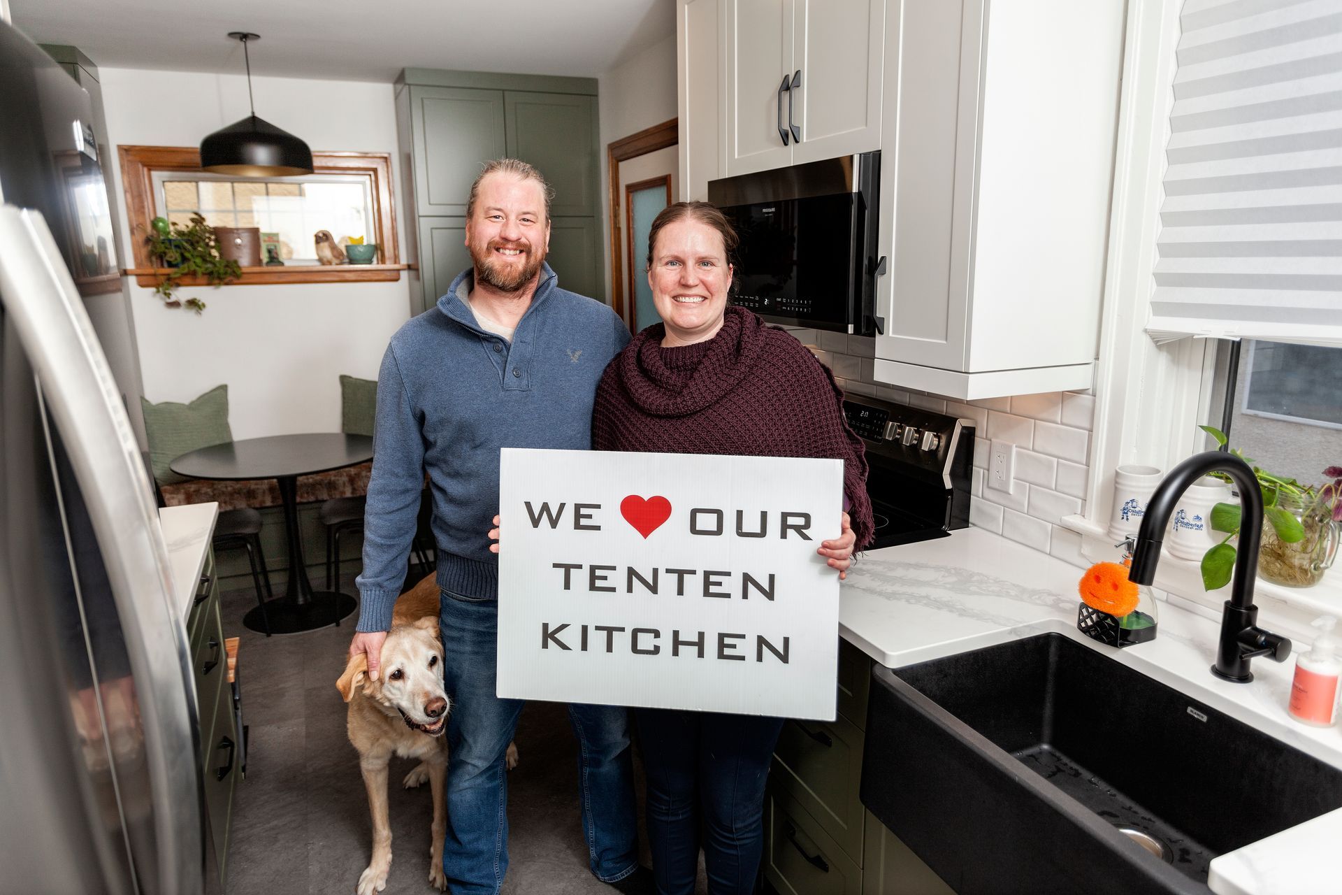 A man and woman are standing in a kitchen holding a sign that says `` we love our tenten kitchen ''.