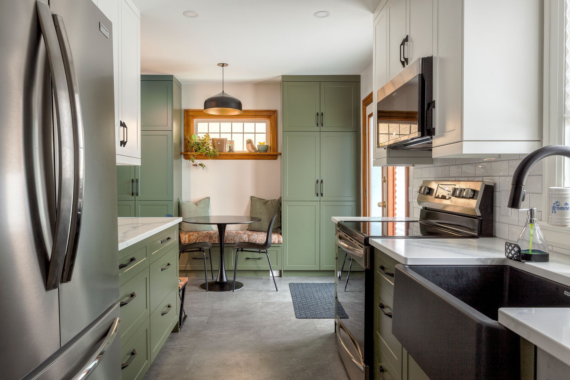 A kitchen with green cabinets , stainless steel appliances , a sink , and a table.