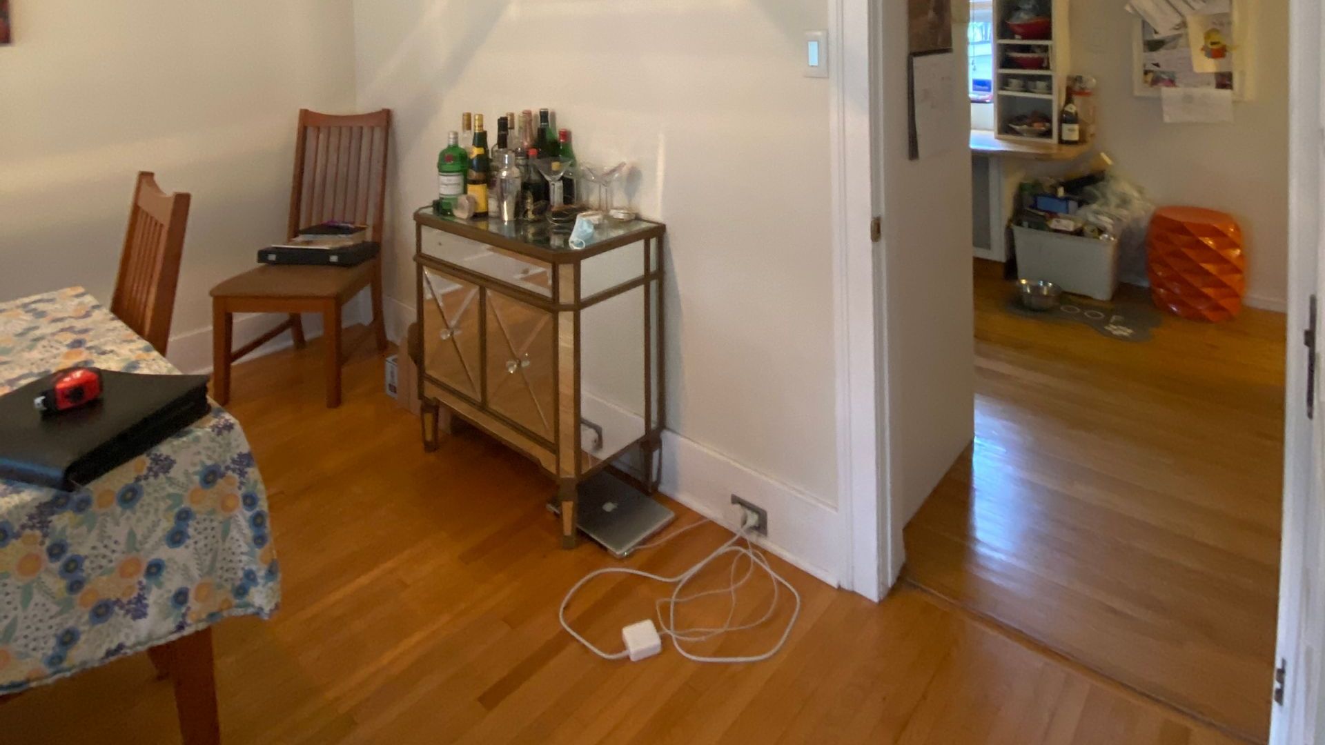 A dining room with a table and chairs and a dresser with bottles on it.