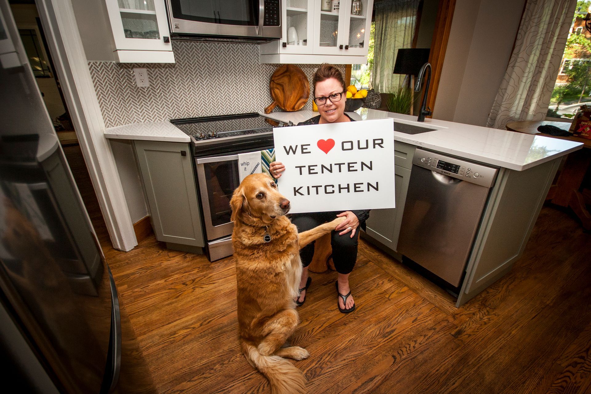 A woman is sitting in a kitchen with a dog holding a sign that says `` we love our tenten kitchen ''.