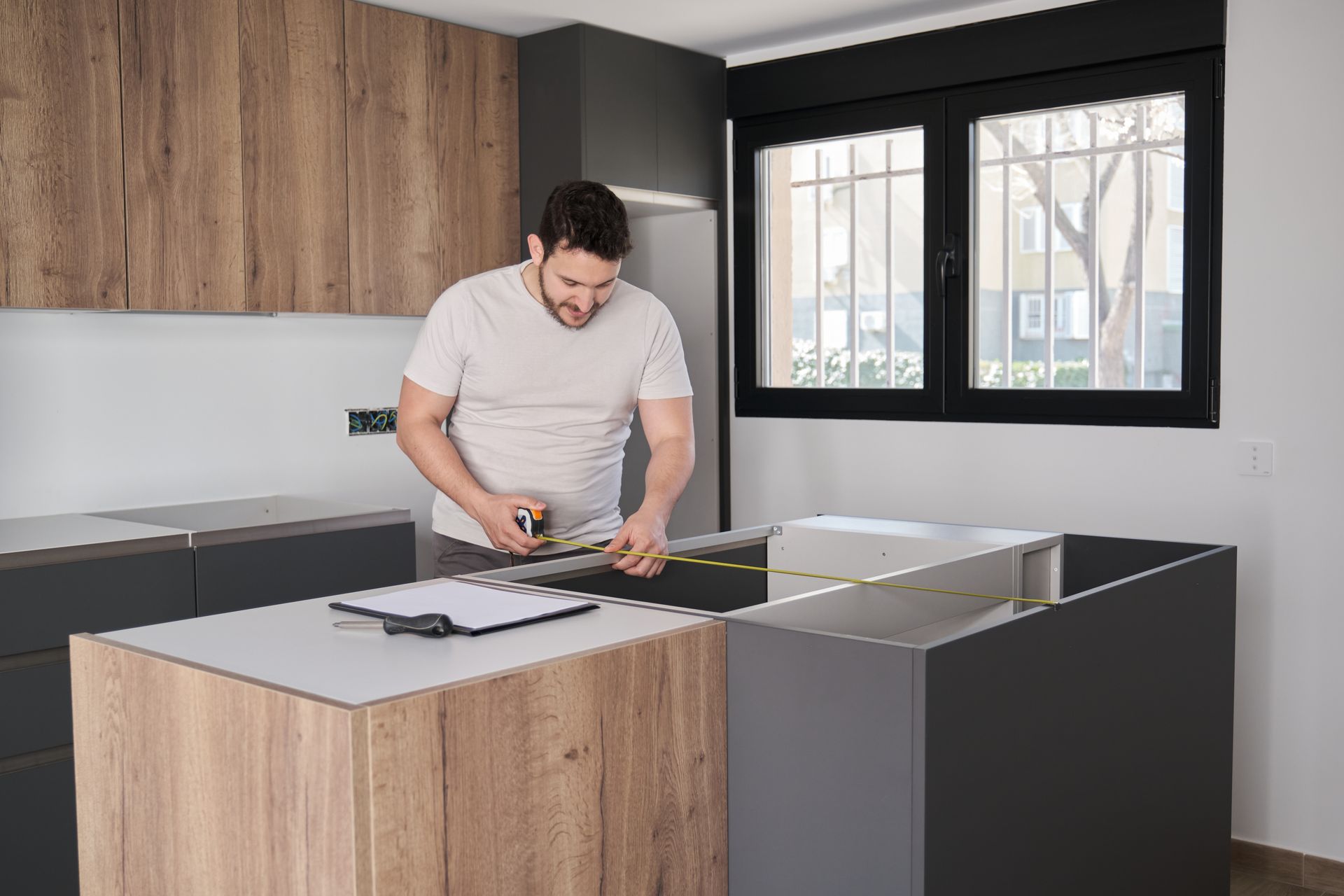 A man is measuring a counter in a kitchen with a tape measure.