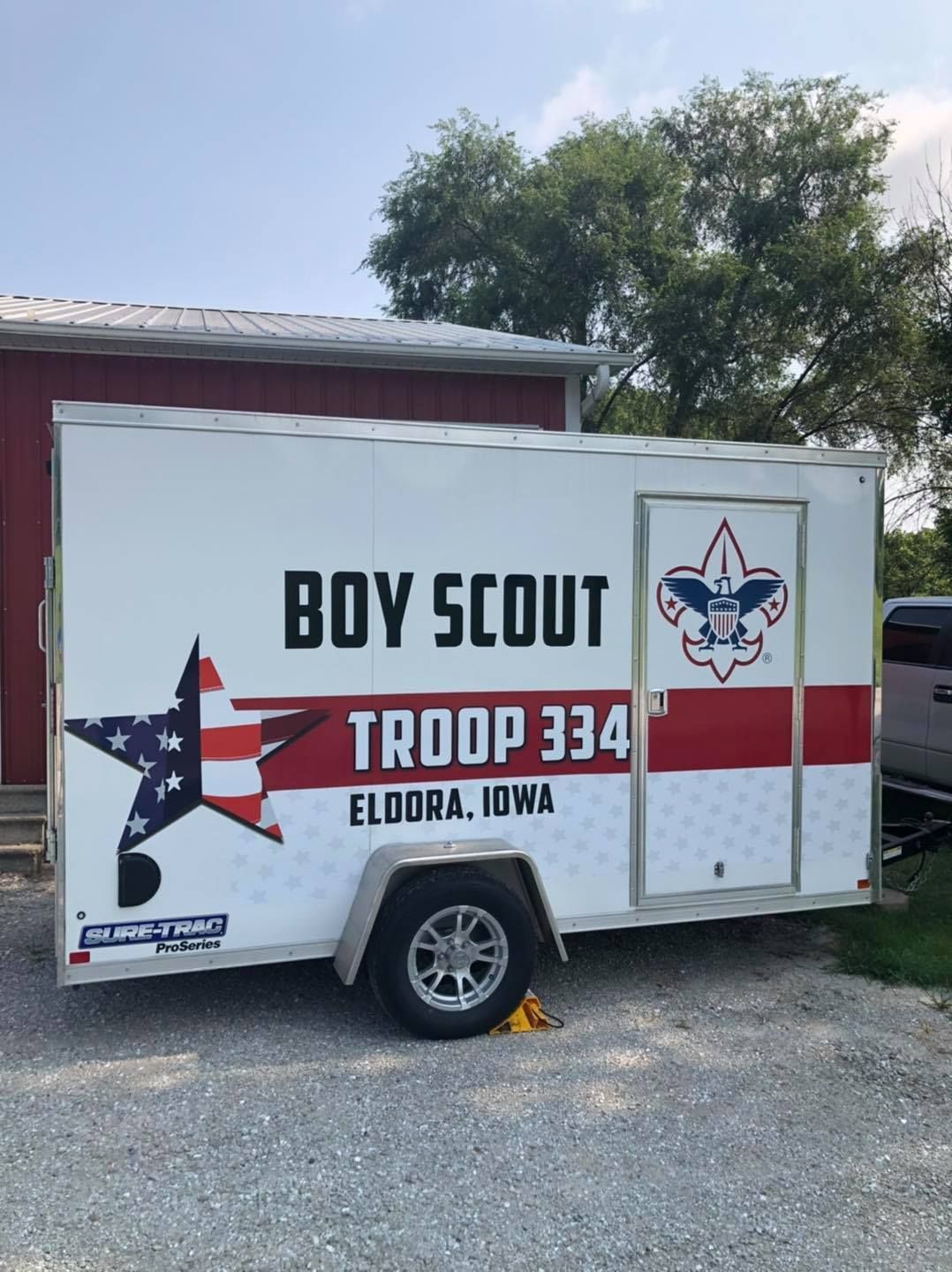 A boy scout trailer is parked in front of a red building.