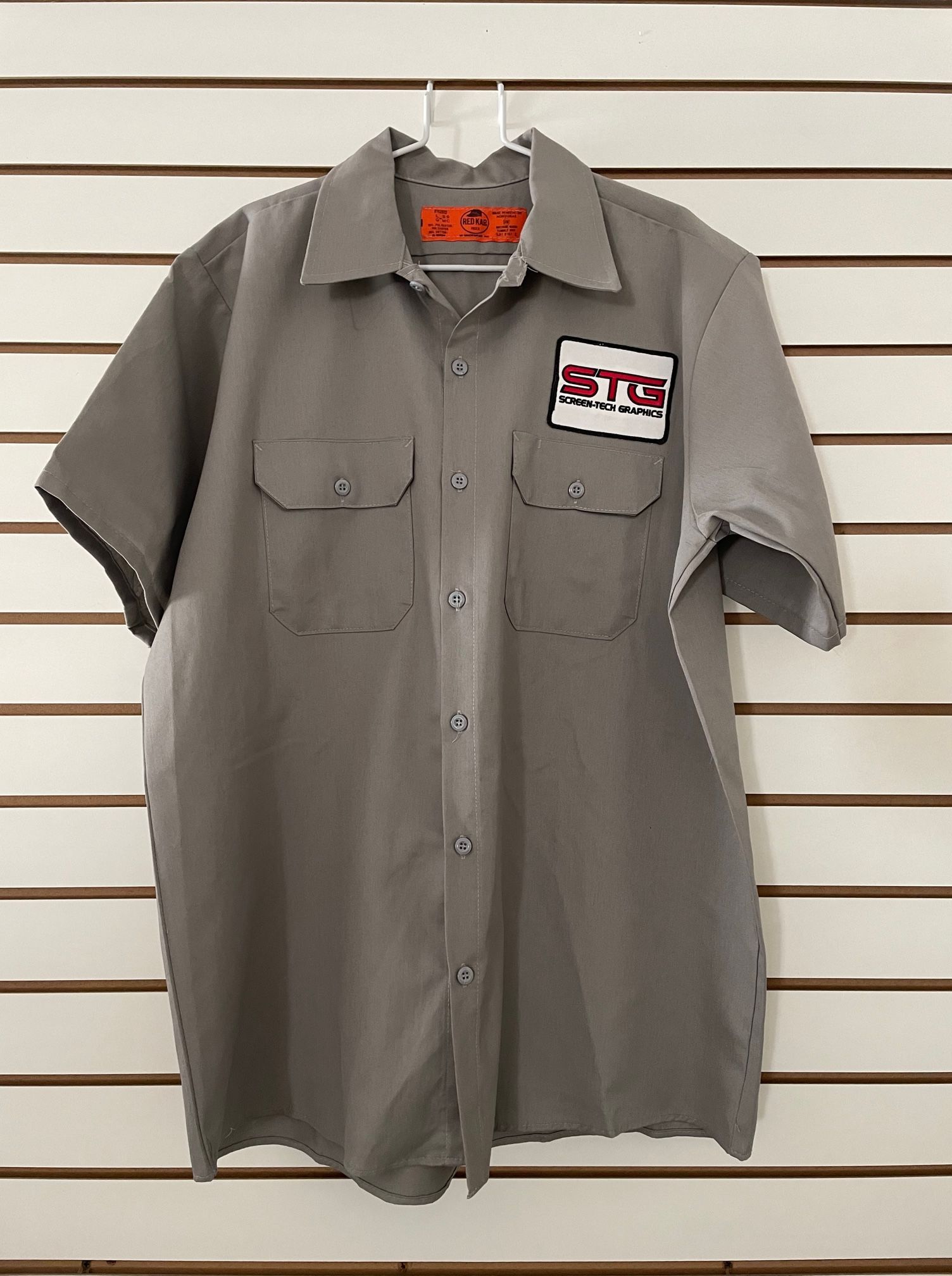 A grey shirt is hanging on a hanger on a wall.