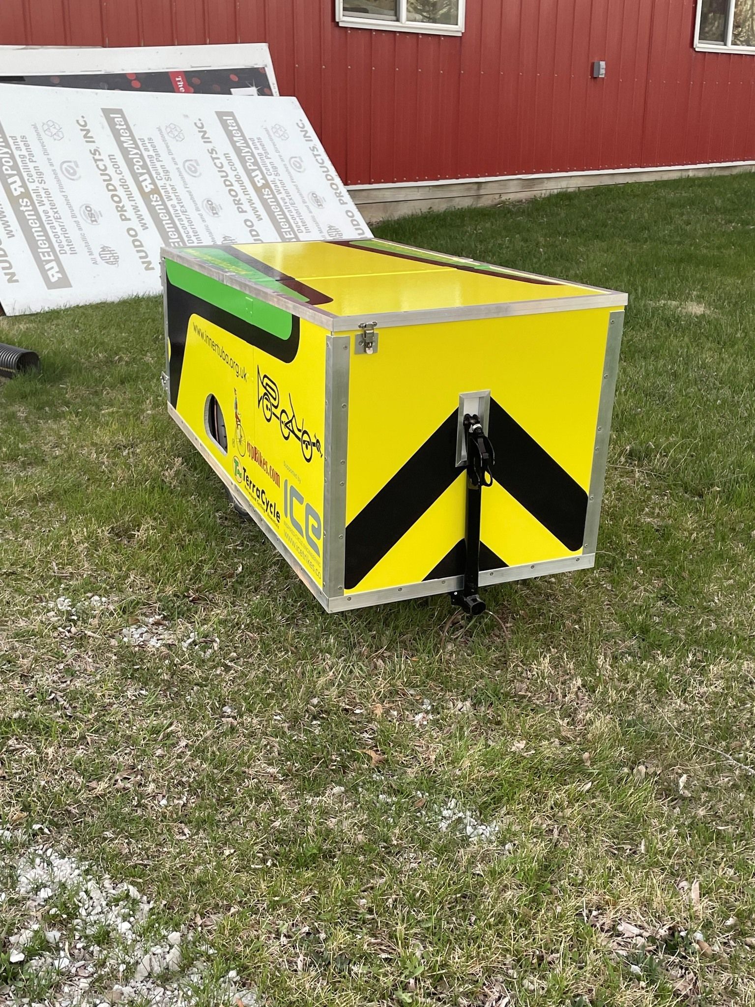 A yellow and black box is sitting in the grass in front of a red building.