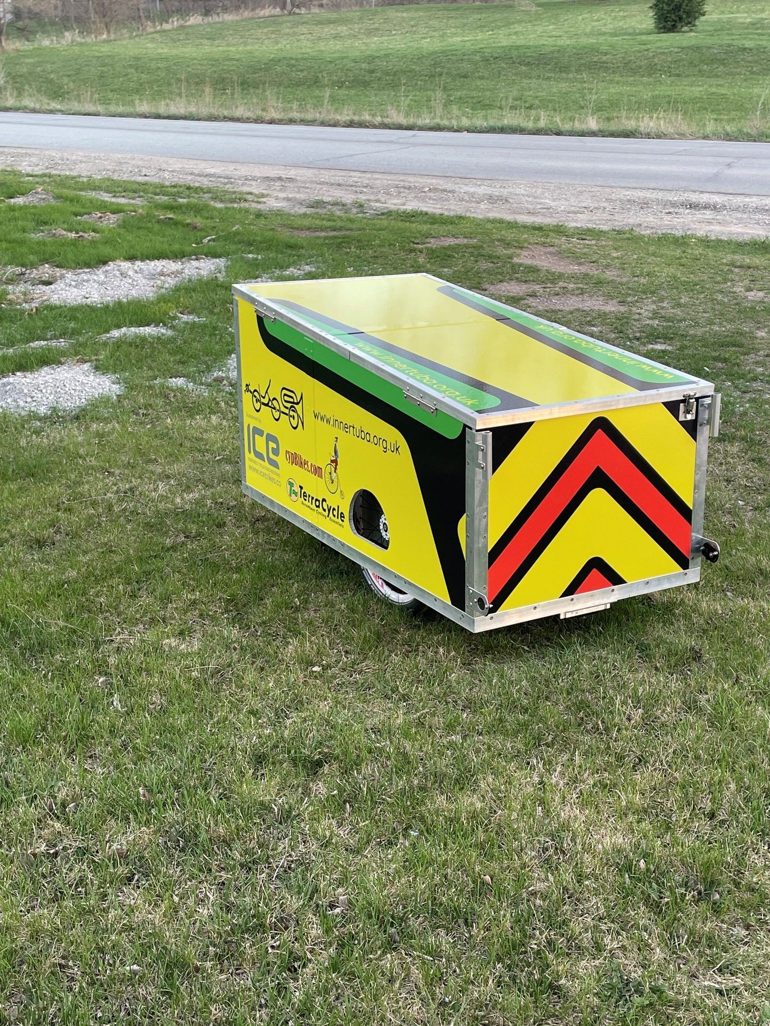 A yellow and green trailer is sitting in the grass next to a road.