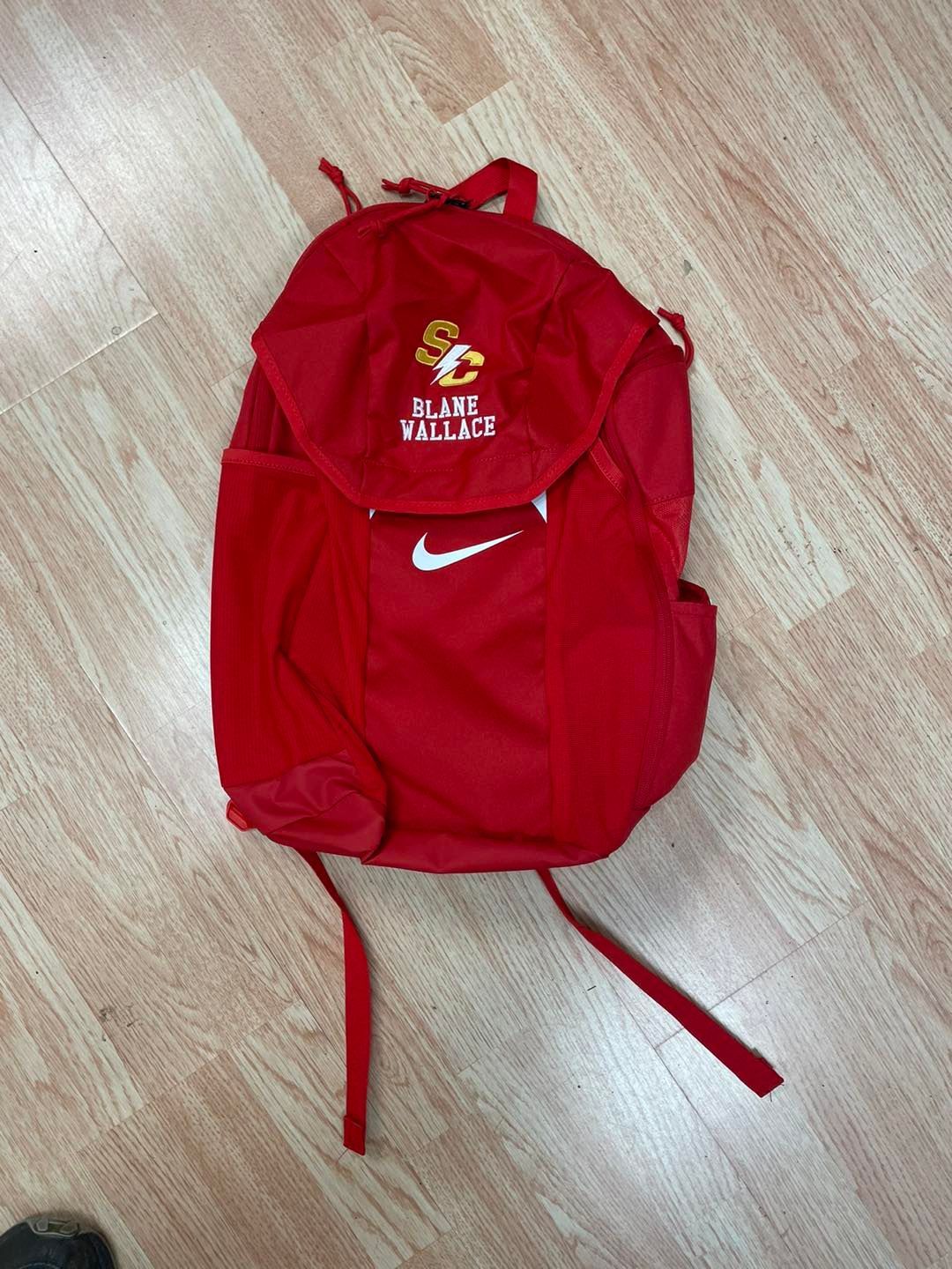 A red nike backpack is sitting on a wooden floor
