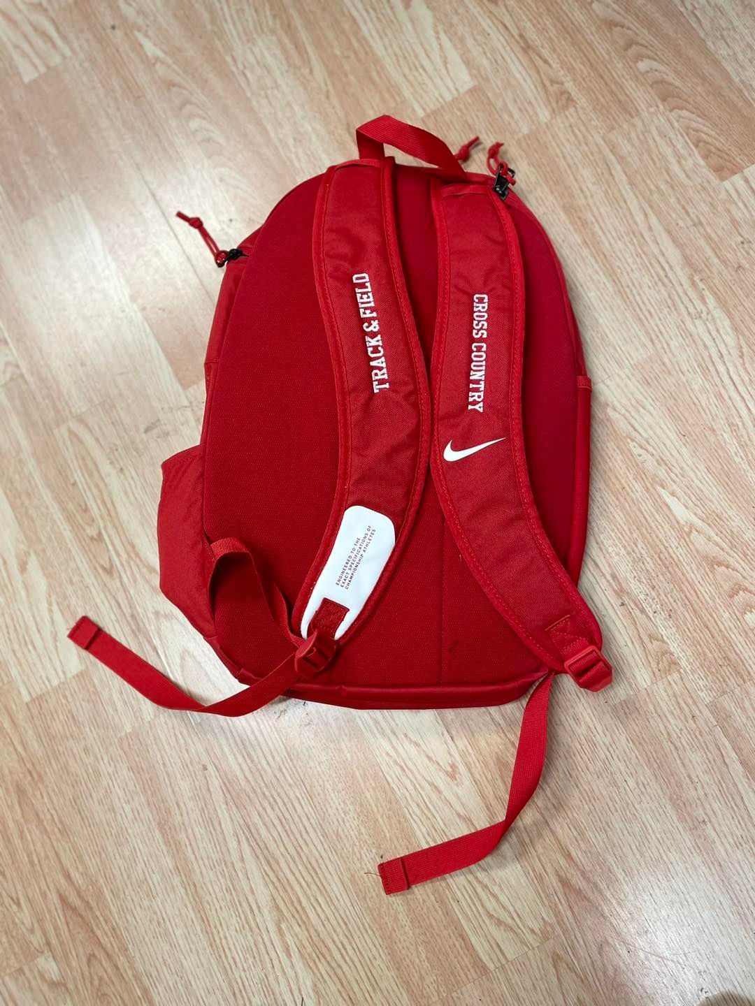 A red nike backpack is laying on a wooden floor