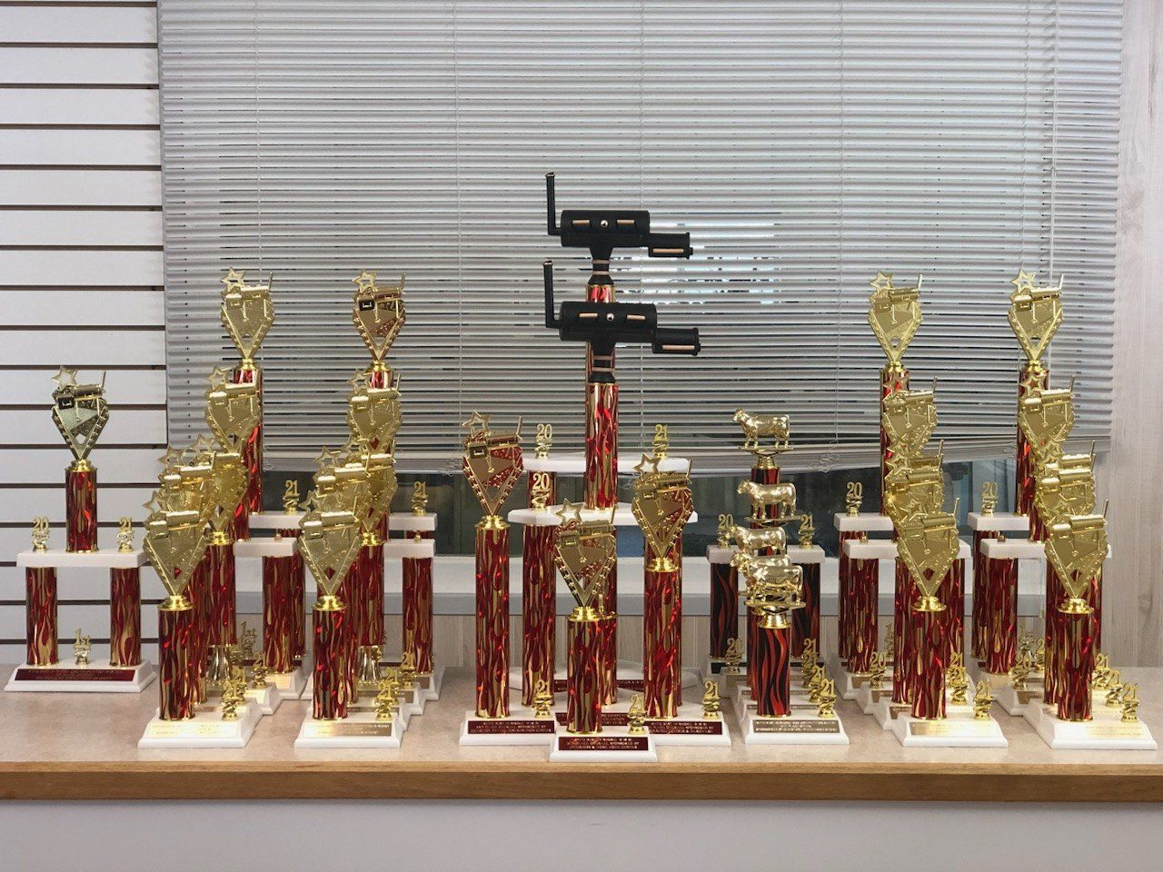 A bunch of trophies are sitting on a table in front of a window.