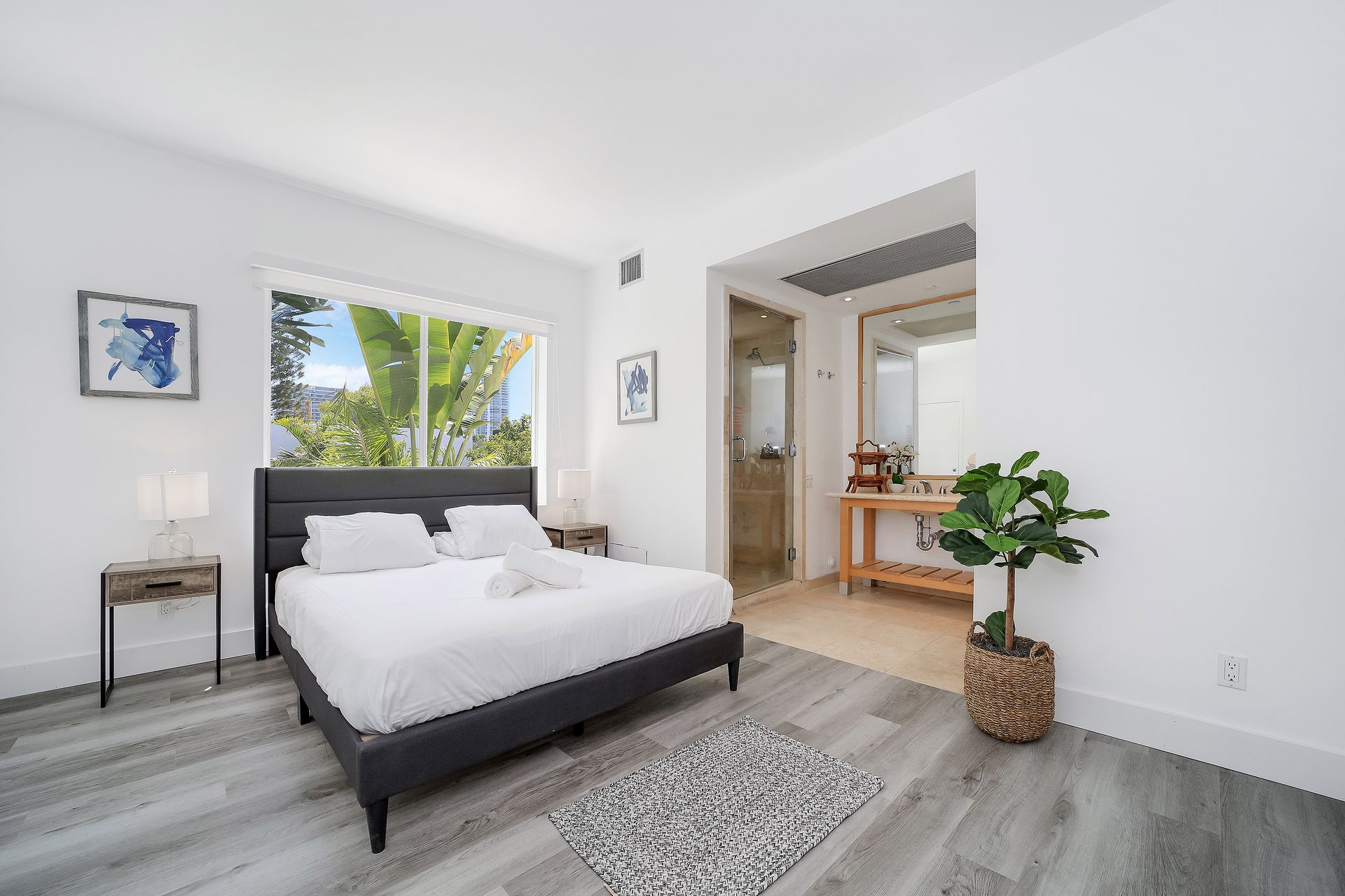 Bedroom with a bed, nightstand, and window overlooking greenery. Bathroom visible through an opening.