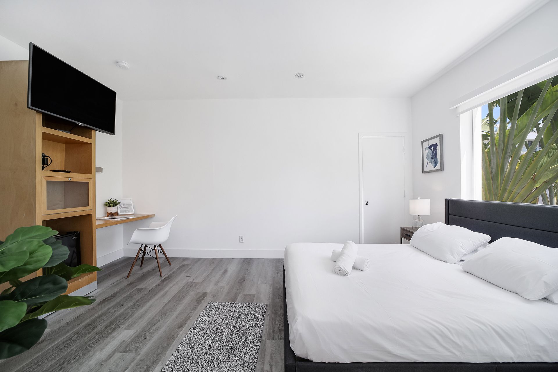 Modern bedroom with a bed, desk, TV, and window with a view of greenery.