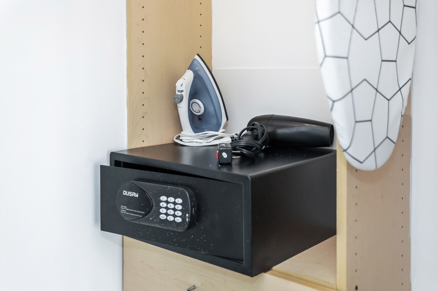 Black safe with open drawer, iron, hairdryer, and ironing board in a closet.