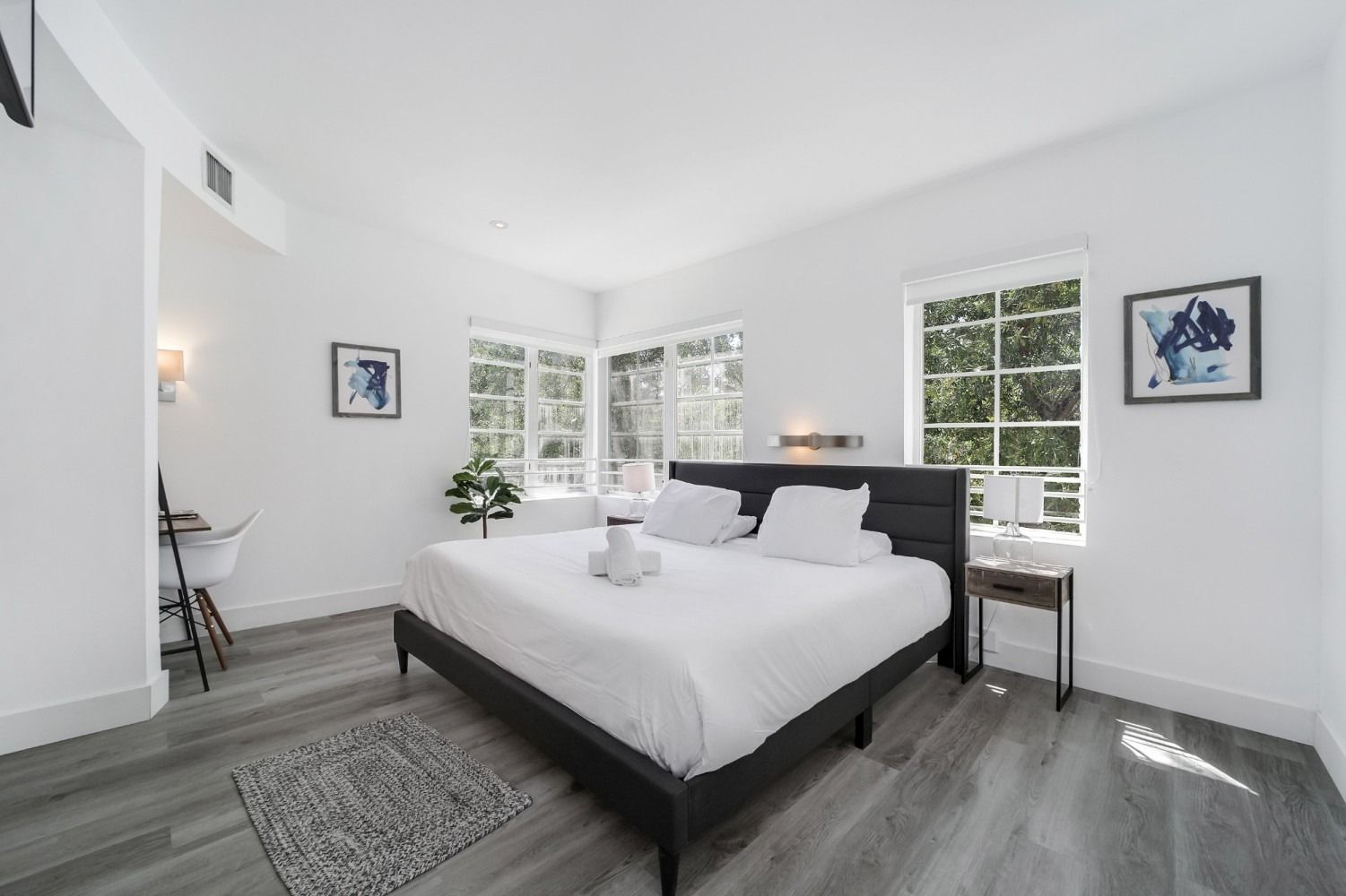 Bright, white bedroom with large bed, gray floors, and windows overlooking greenery.