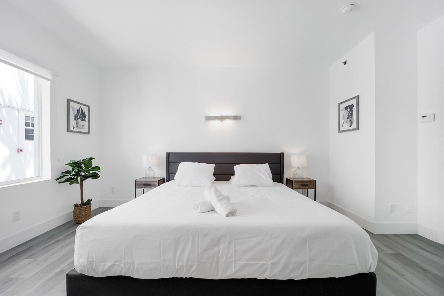 Bright white bedroom with a large bed, two nightstands, and a small plant.