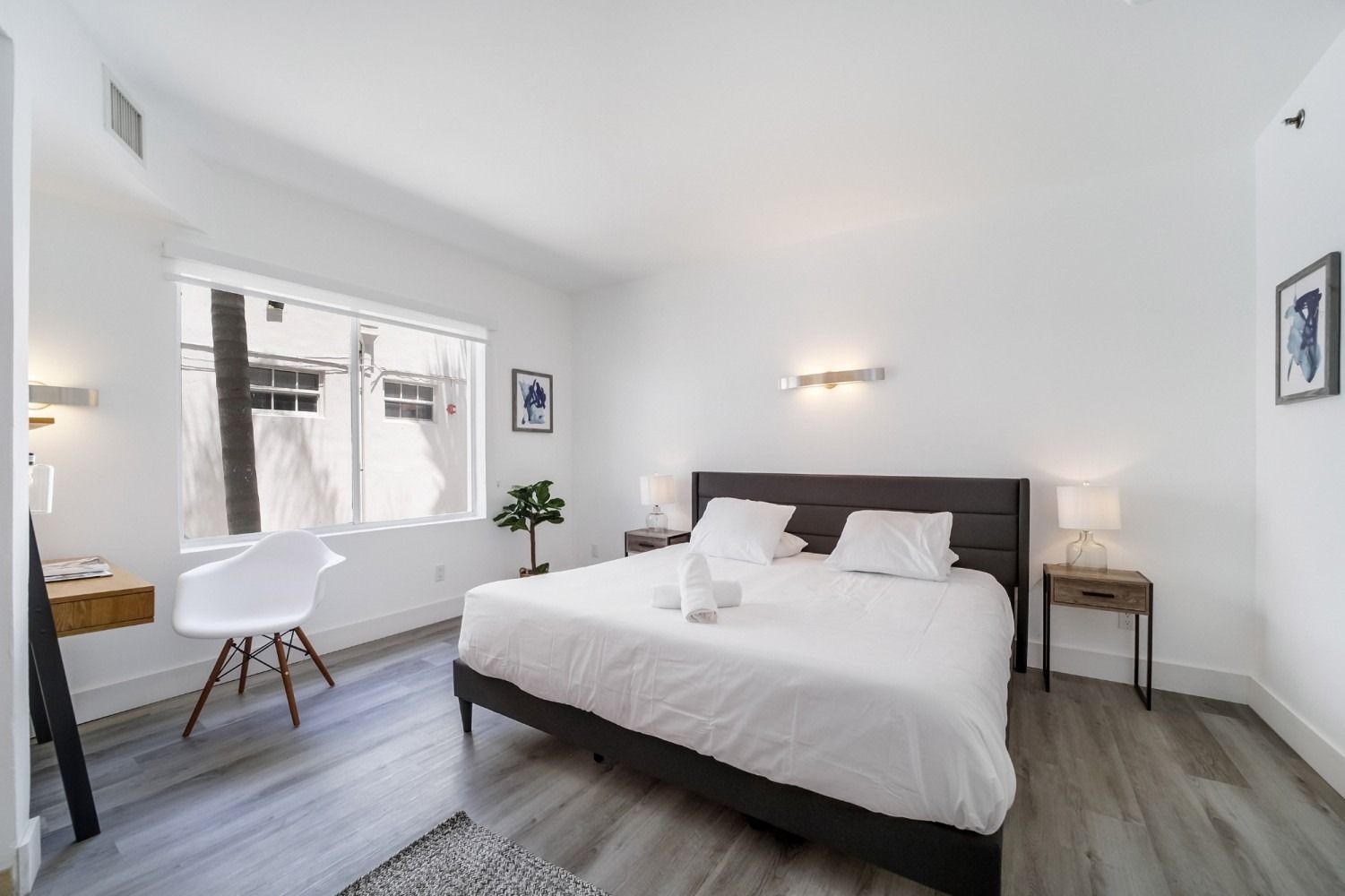Bedroom with white walls, large bed, small desk, and window.