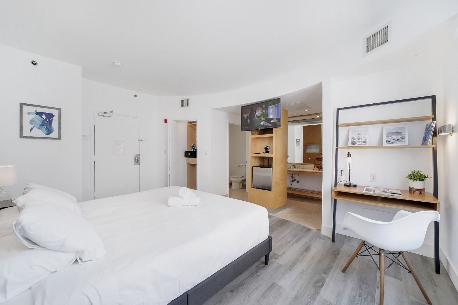 Hotel room interior with bed, desk, TV, and bathroom entrance. Bright, modern design.