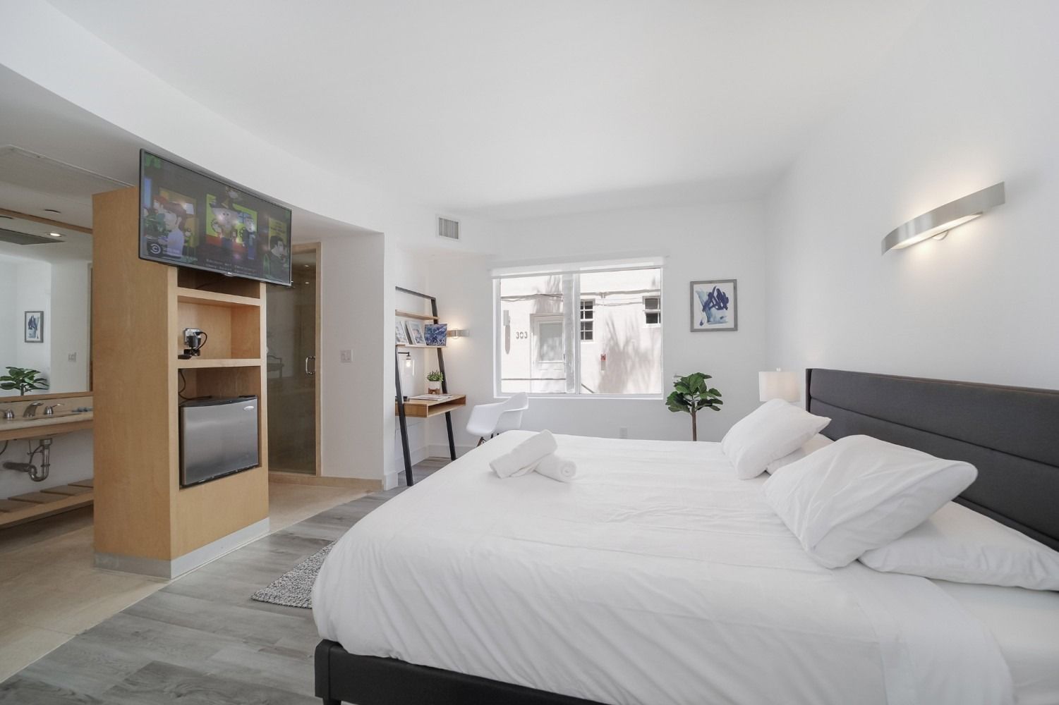 Bedroom with a white bed, desk, and a window. A small refrigerator is in a cabinet.