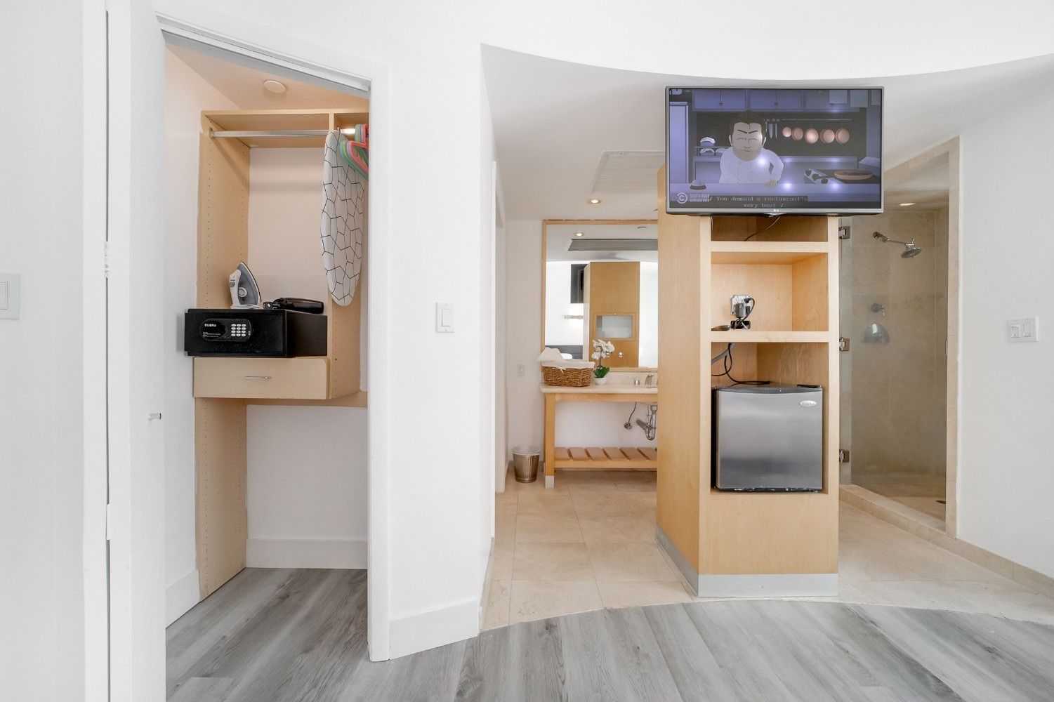 Interior view of a hotel room with a closet, bathroom, and a TV mounted on a shelf with a mini-fridge.
