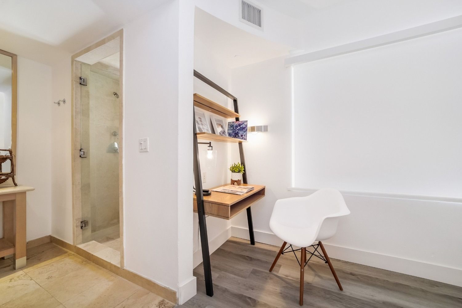 Modern bedroom with shower, desk, and white chair. Bright white walls, wood floors.