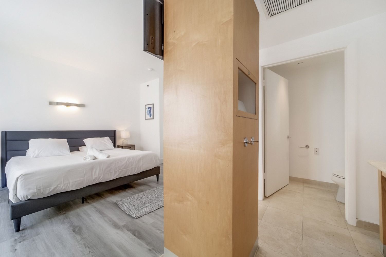 Bedroom with bed, and doorway to bathroom. Wooden column in view. White walls.