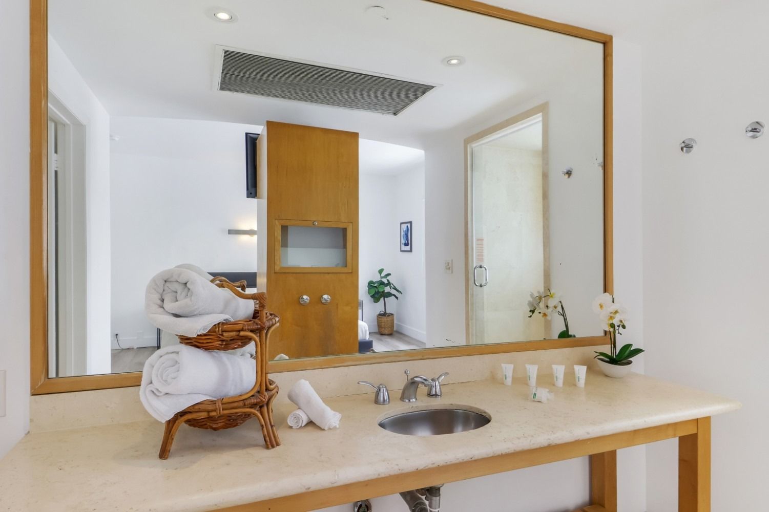 Bathroom with large mirror, sink, and rolled towels on a wooden counter.