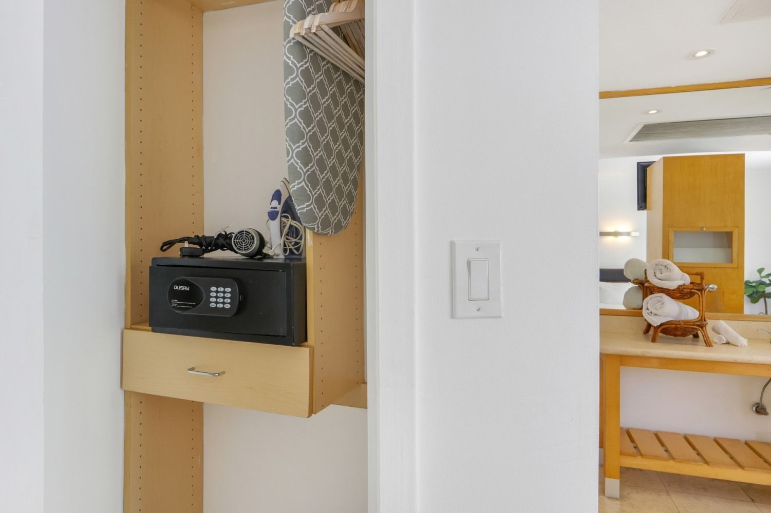 Closet with built-in safe, drawer, ironing board, and open doorway to a bathroom with towels.