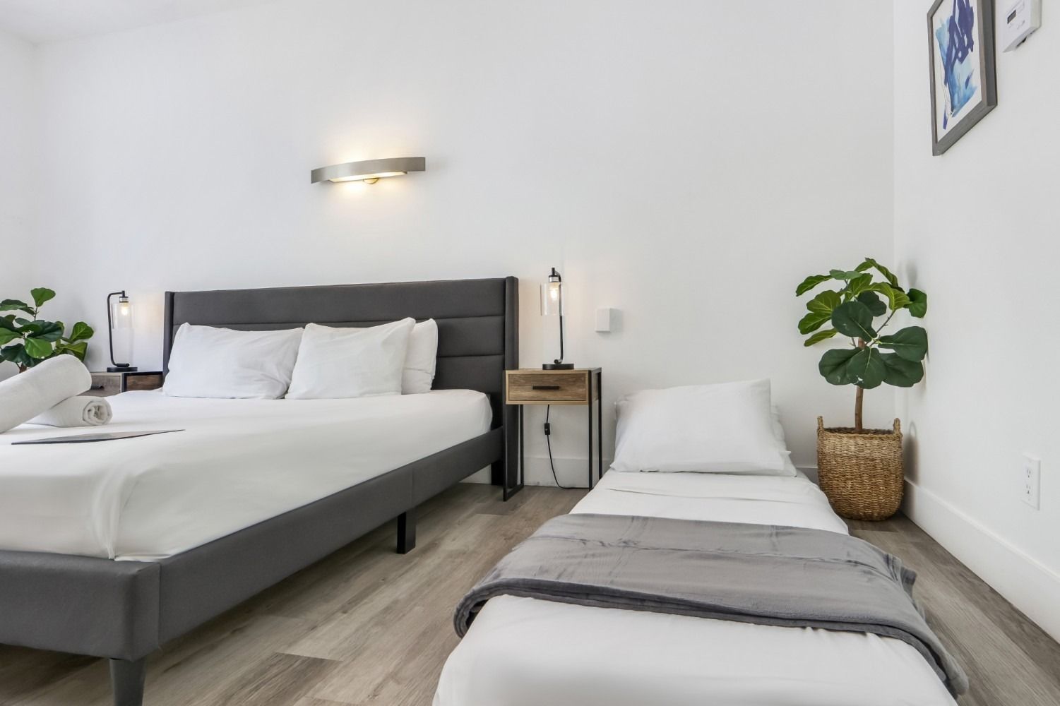 Bedroom with queen bed, pull-out bed, nightstand, plants, and gray and white decor.
