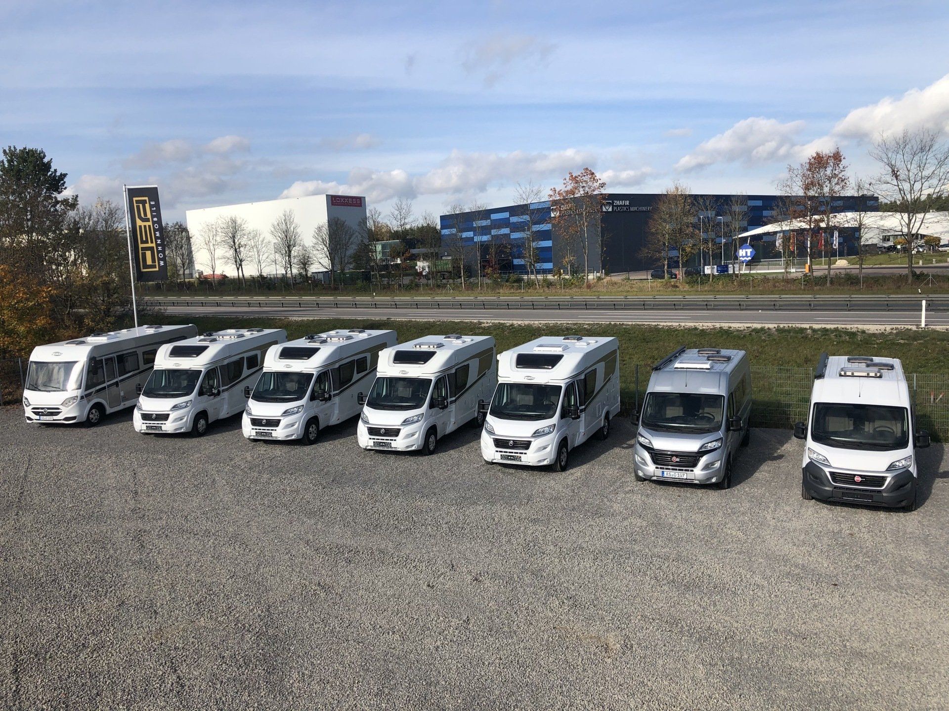 Eine Reihe Wohnmobile sind auf einem Schotterplatz geparkt.