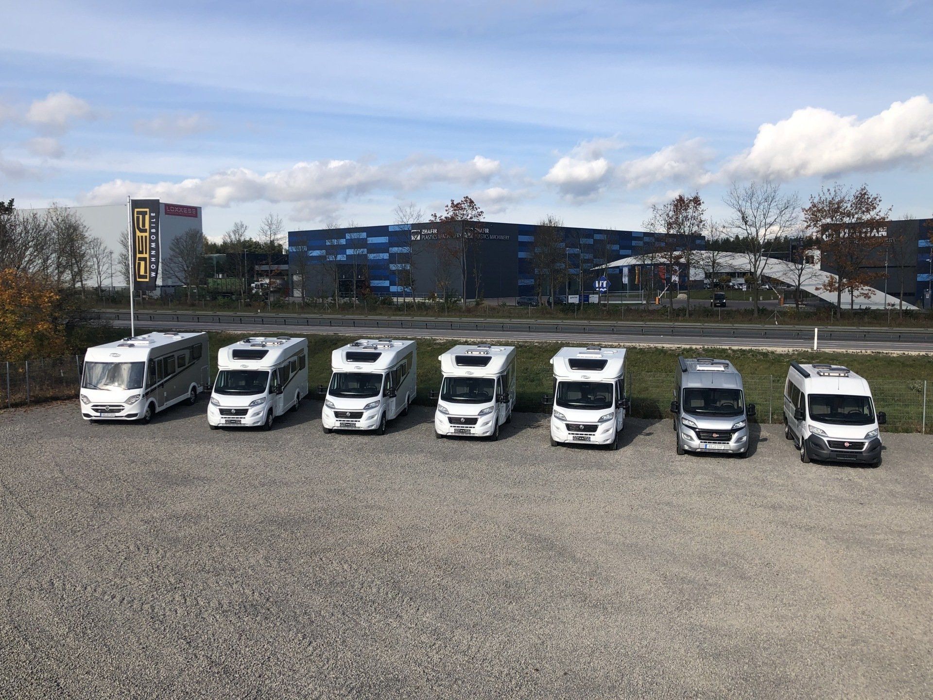 Eine Reihe Wohnmobile sind auf einem Schotterplatz geparkt.