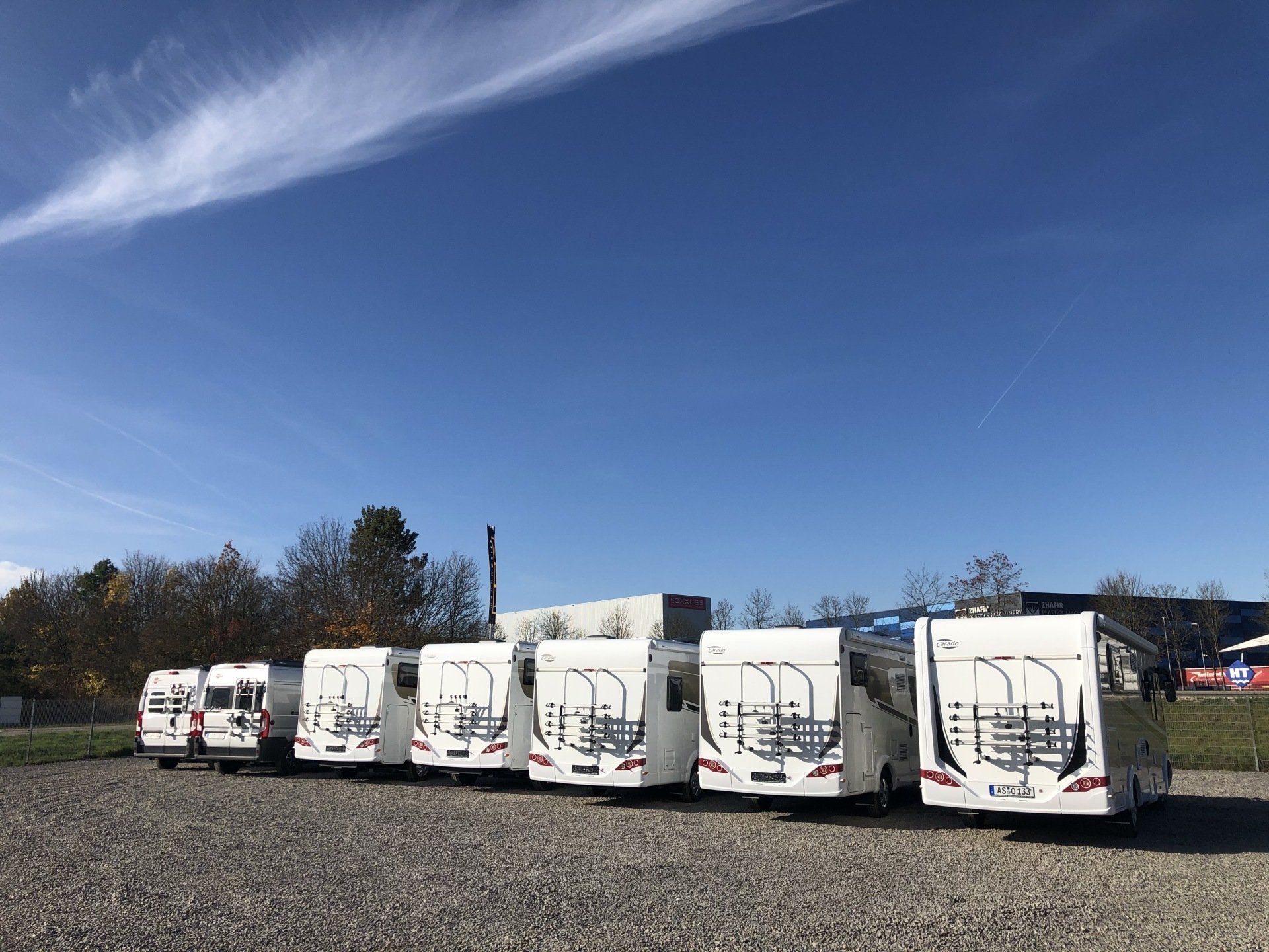 Eine Reihe weißer Wohnmobile steht auf einem Schotterplatz.