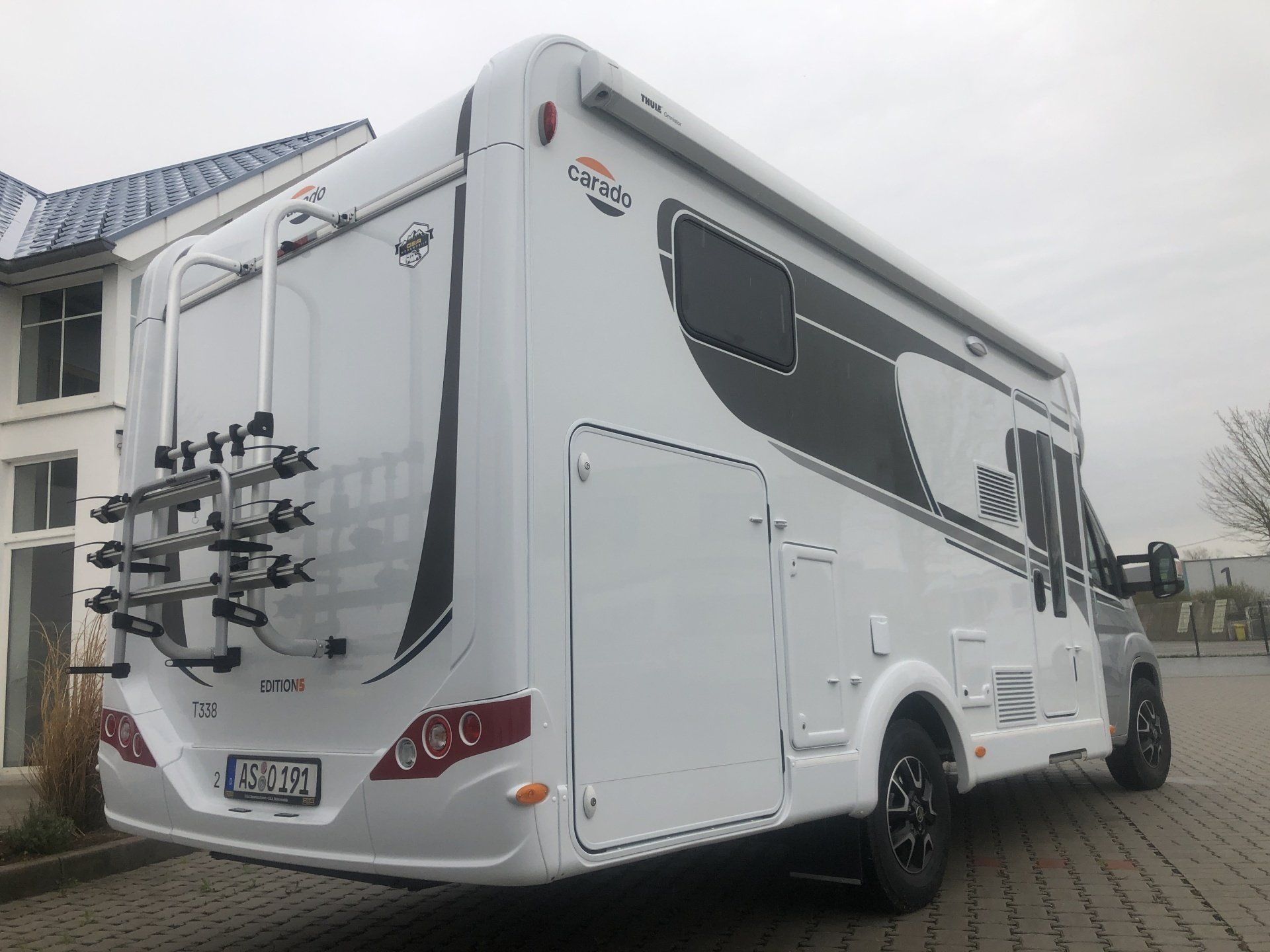 A white rv with a bike rack on the back is parked in front of a building.