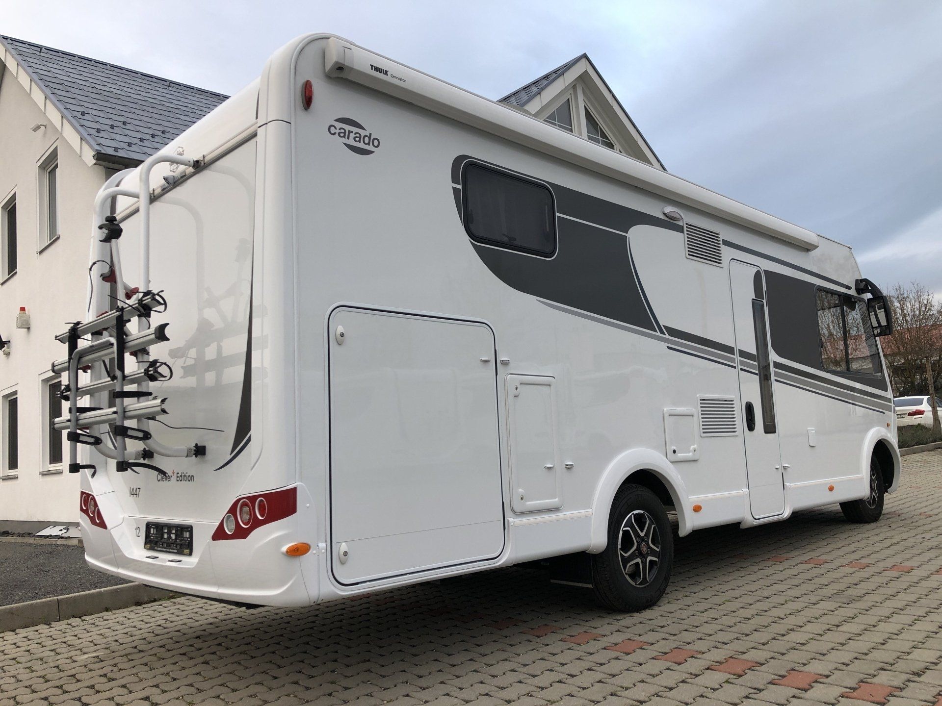 Ein weißes Wohnmobil mit einem Fahrradträger auf der Rückseite ist vor einem Haus geparkt.
