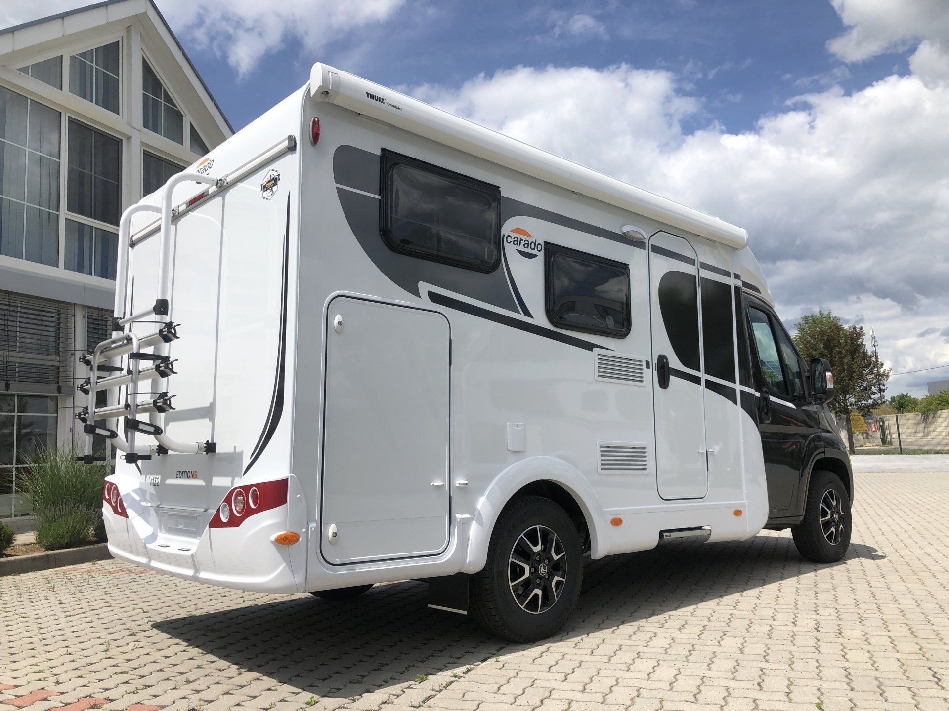 A white and black rv is parked in front of a building.