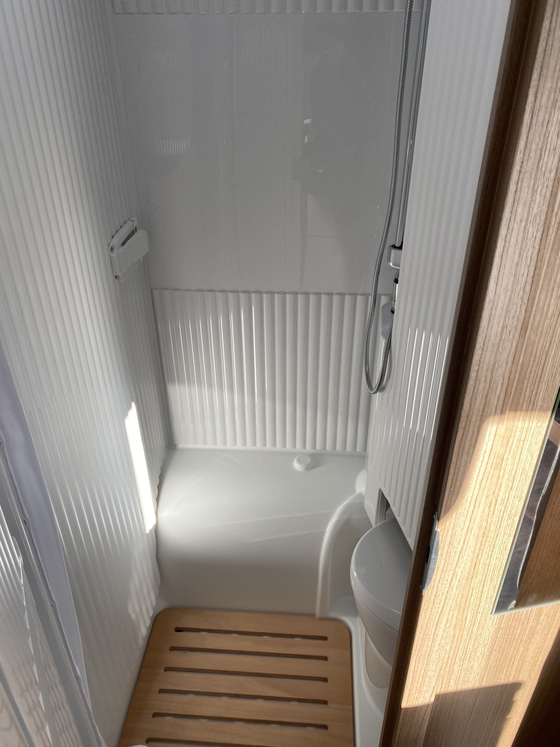 A bathroom with a shower , toilet , and wooden floor.