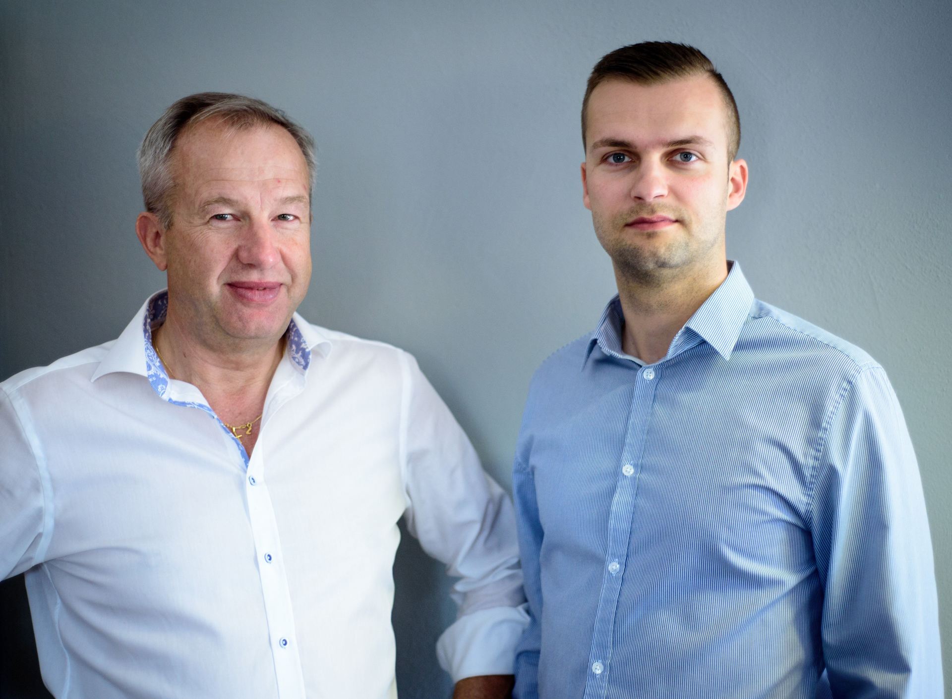 Zwei Männer stehen nebeneinander vor einer Wand.