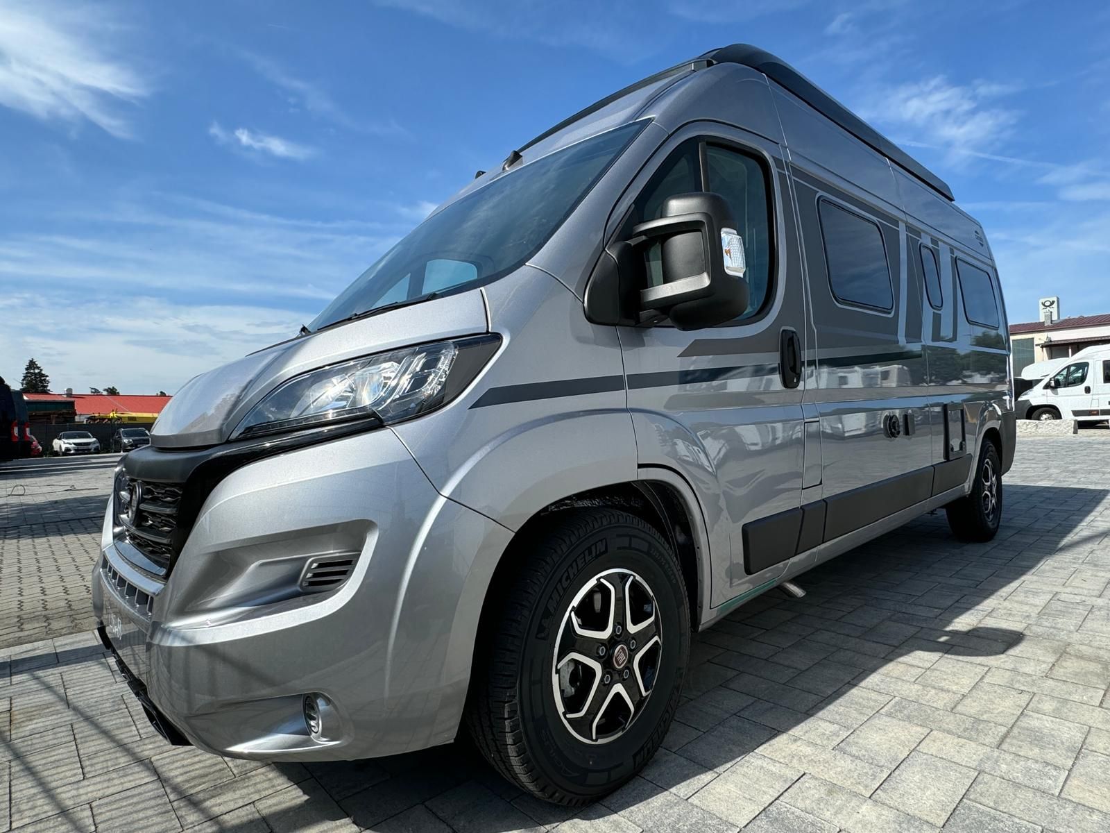 Ein silberner Campervan parkt an einem sonnigen Tag draußen.