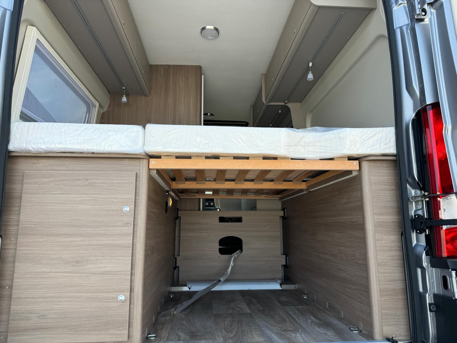 Innenansicht eines Wohnmobils mit Bett, Stauraum und freiliegenden mechanischen Bauteilen.