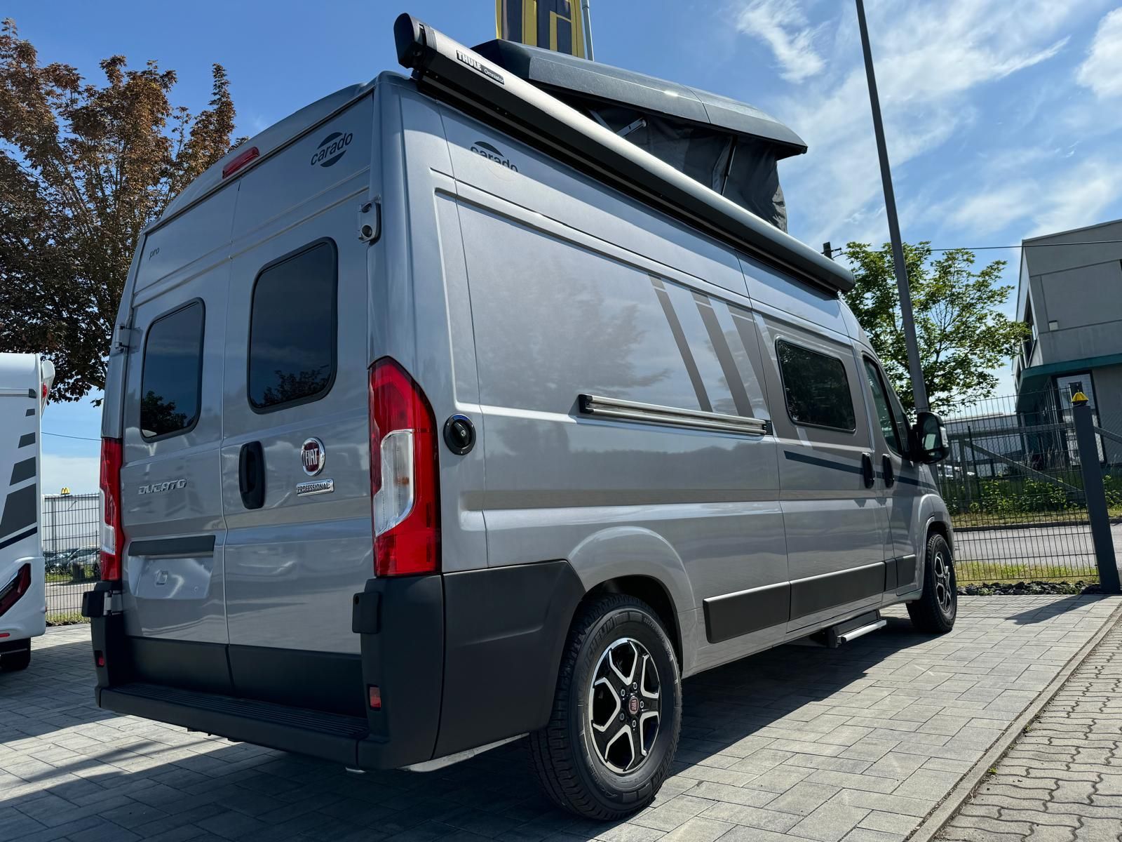 Grauer Campervan mit schwarzen Akzenten und Aufstelldach parkt auf dem Bürgersteig.