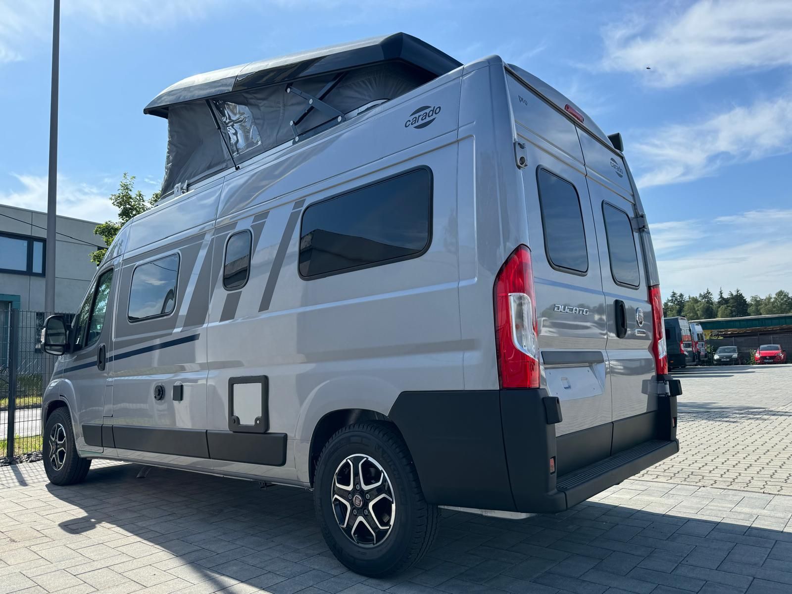 Silberner Camper mit Hochdach, der an einem sonnigen Tag draußen parkt.