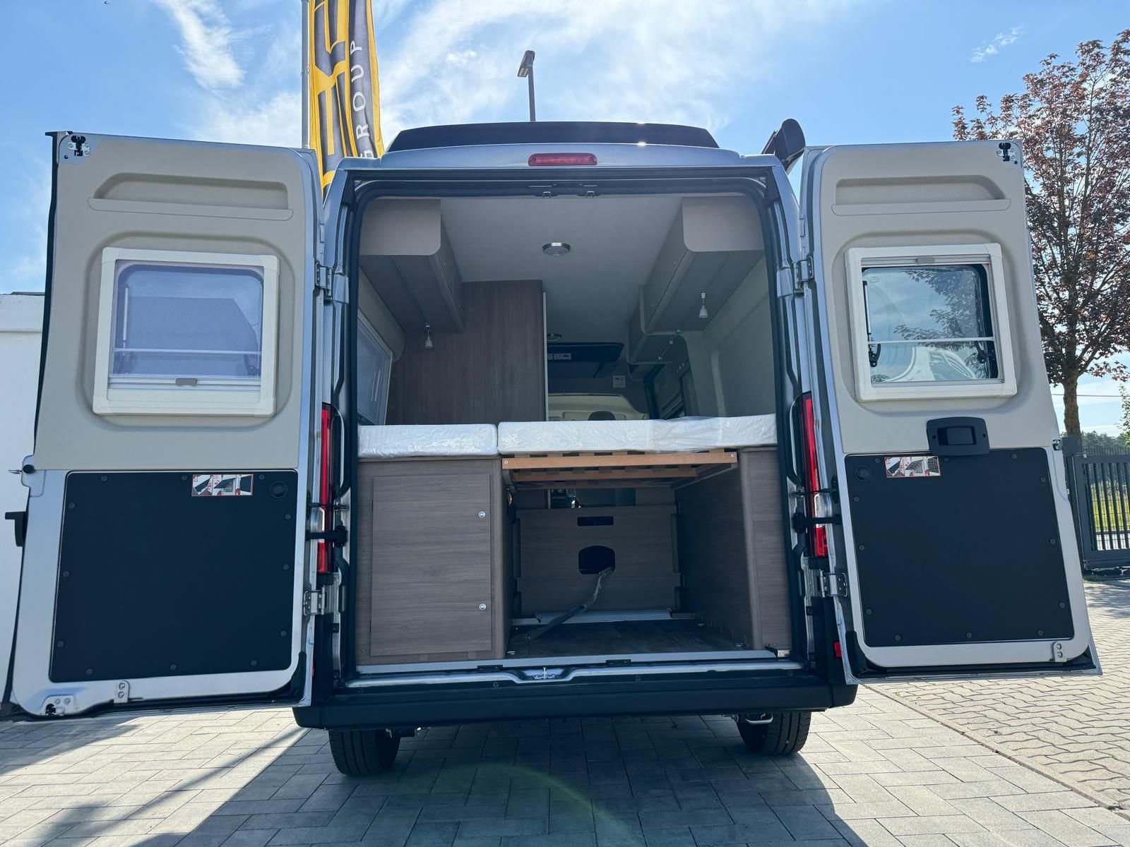 Rückansicht eines Wohnmobils mit geöffneten Türen, die einen Innenraum mit Bett und Stauschränken freigibt.