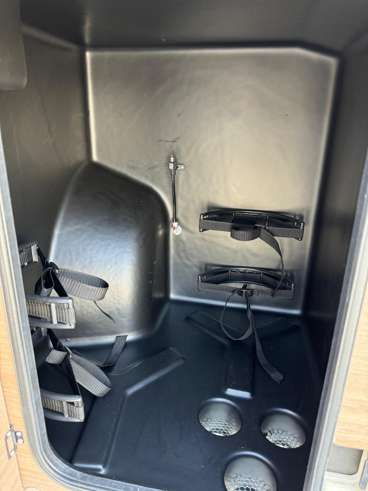Innenstaufach mit schwarzen Kunststoffoberflächen, Gurten und runden Löchern.