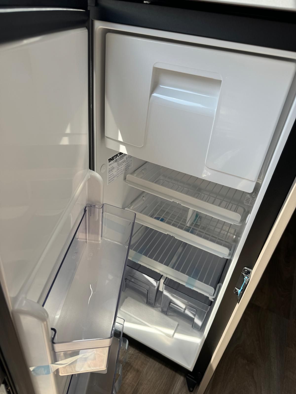 Offener, leerer Wohnmobil-Kühlschrank mit zwei Ablagen und einem Gefrierfach.