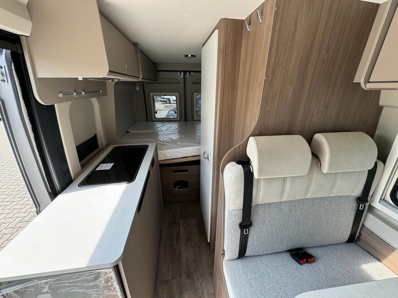 Innenansicht eines Wohnmobils mit Küchentheke, Sitzgelegenheiten und Stauschränken.