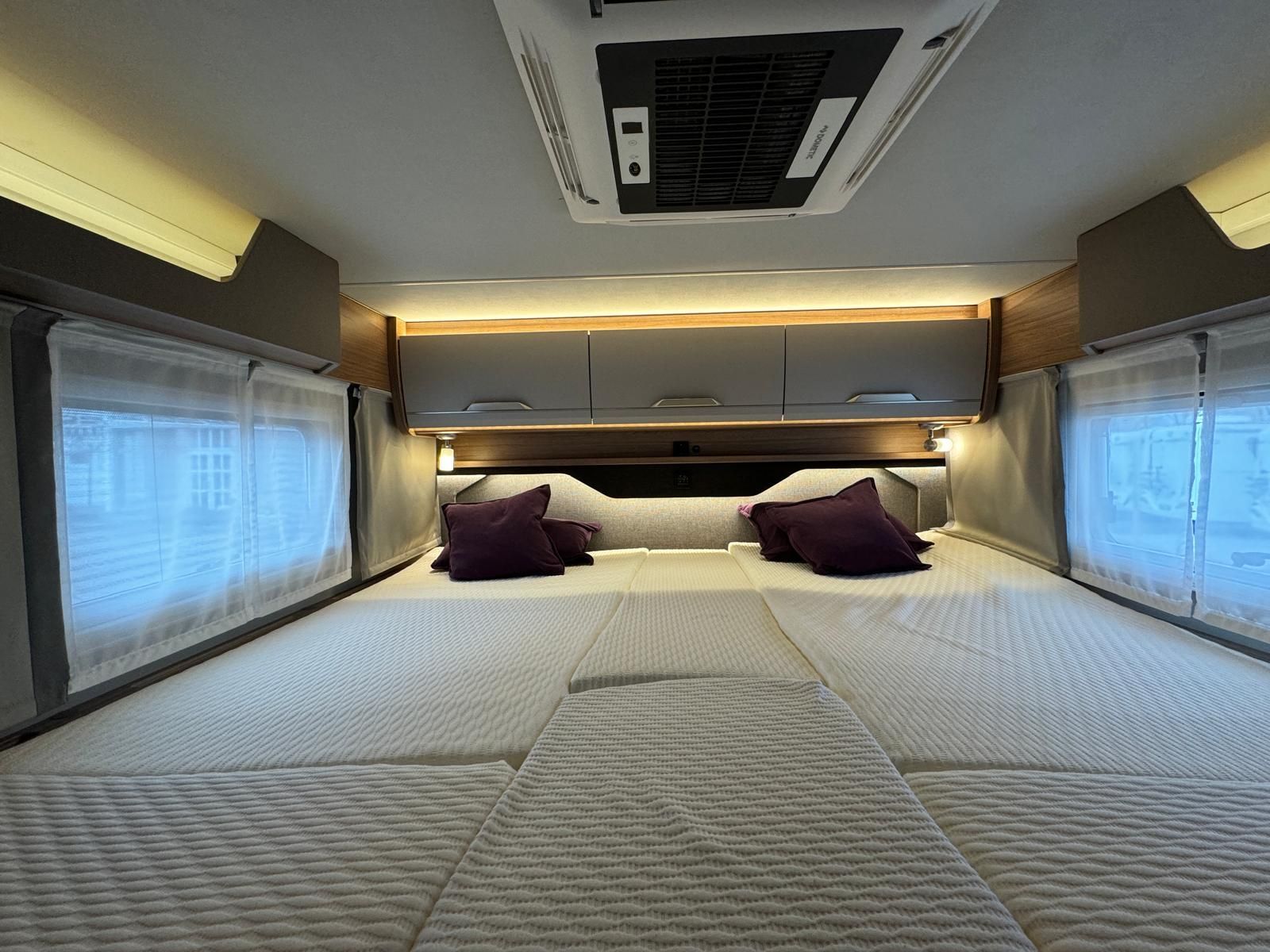 Ein Bett in einem Wohnmobil mit lila Kissen und einem Deckenventilator.