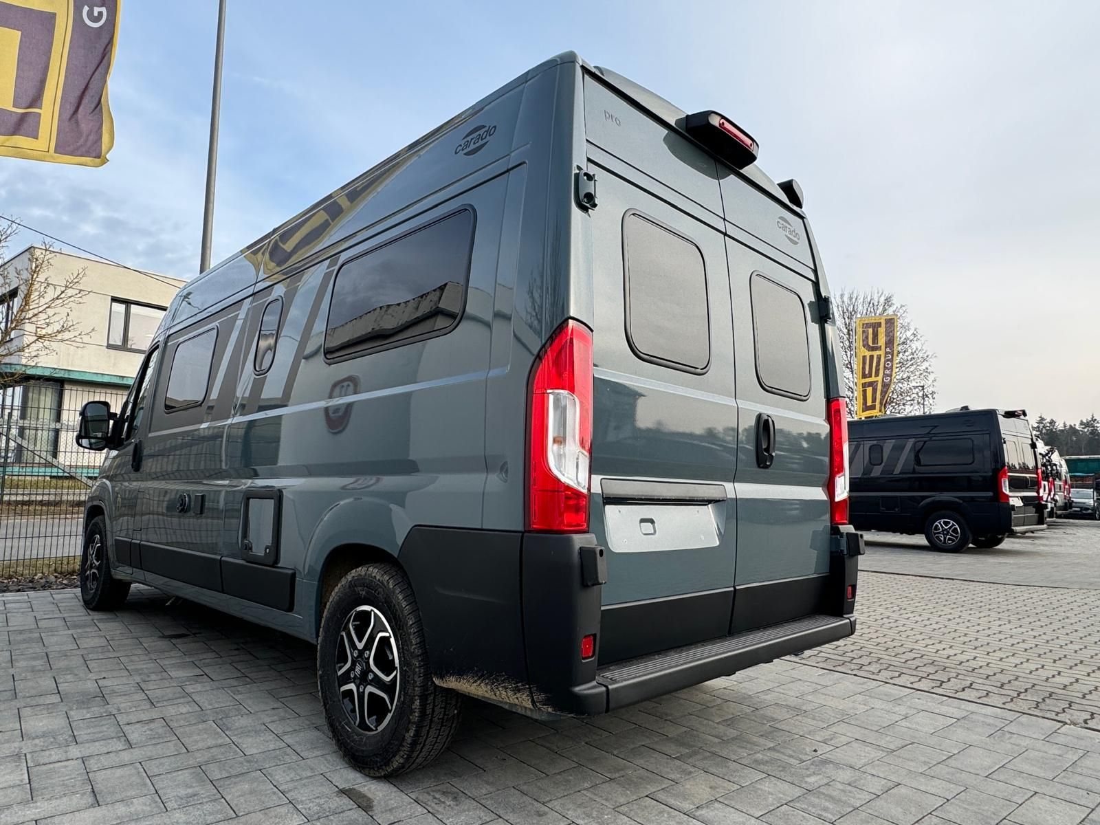 Ein grauer Wohnwagen steht im Freien auf einem gepflasterten Parkplatz. 