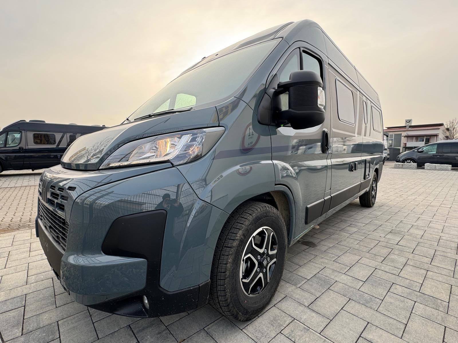 Grauer Wohnwagen, der im Freien auf einer Ziegelfläche parkt.