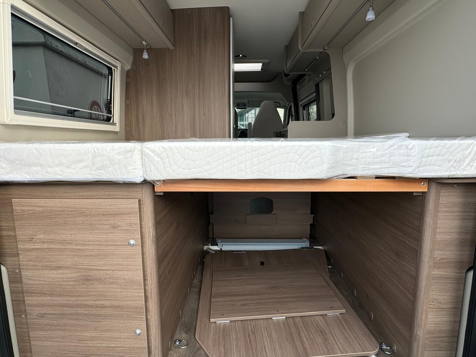 Innenraum eines Wohnmobils mit einer Schlafplattform über Staufächern. Holzschränke und offener Raum.