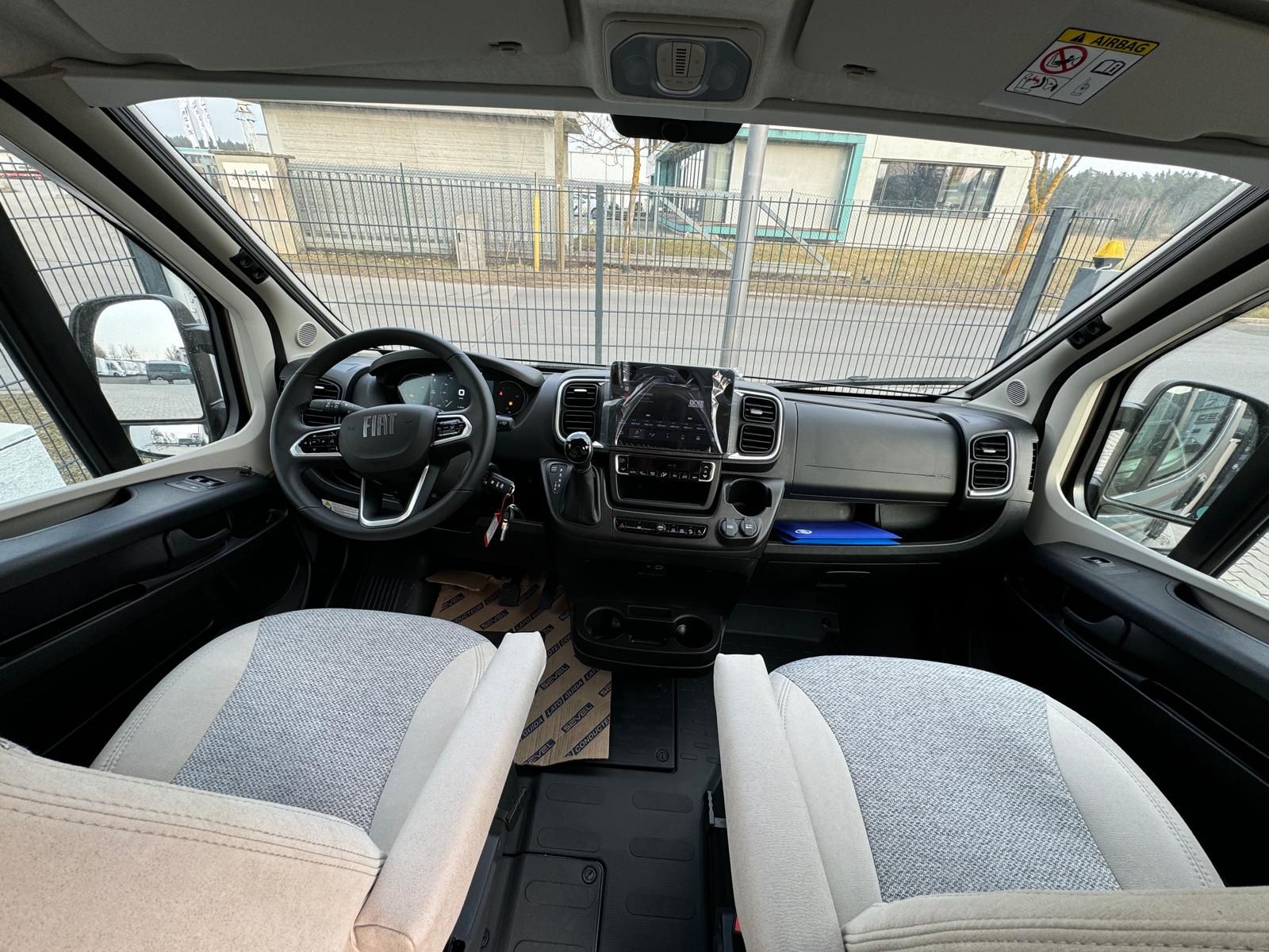 Innenansicht eines Wohnmobils mit Armaturenbrett, Lenkrad, Sitzen und geöffneten Türen.