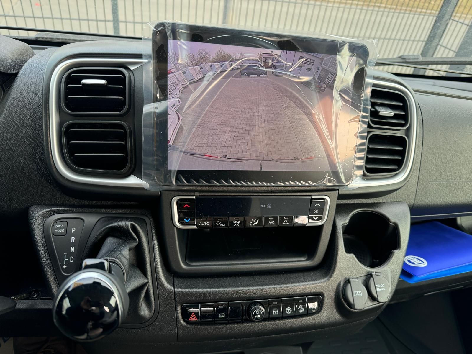 Armaturenbrett mit großem Bildschirm zur Anzeige der Rückfahrkamera. Schalthebel links, Getränkehalter rechts.