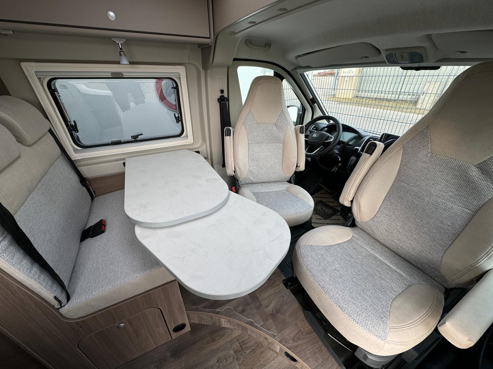Innenraum eines Wohnmobils mit Sitzen, Tisch und Fenster.