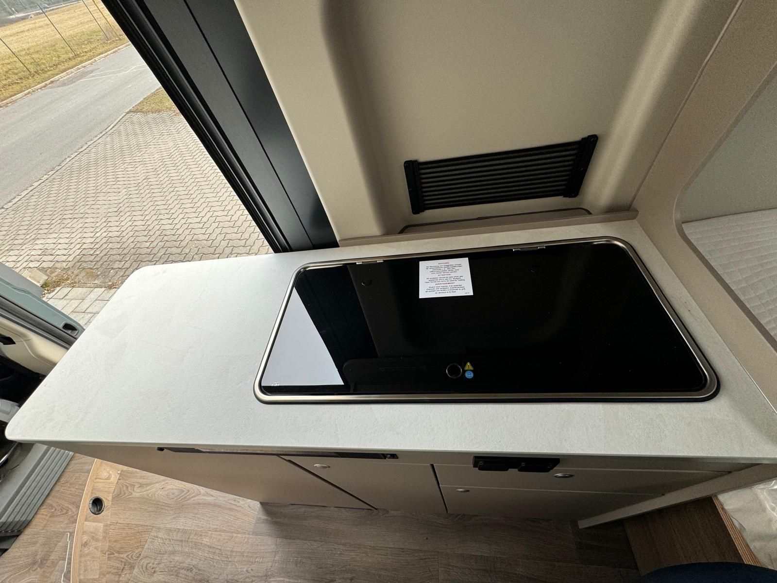 Innenansicht einer Wohnmobilküche mit Kochfeld, Arbeitsfläche und Stauraum.